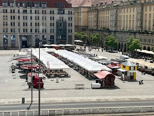 Blick von oben auf den Dresdner Altmarkt mit langen Reihen weißer Marktzelte und Verkaufsständen. Im Hintergrund befinden sich helle, mehrstöckige Gebäude der Innenstadt an einem sonnigen Tag.