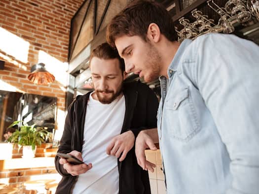 Zwei Männer betrachten gemeinsam ein Smartphone in einem Café
