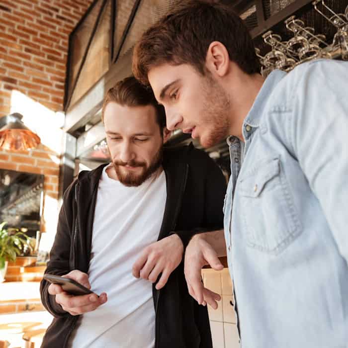 Zwei Männer betrachten gemeinsam ein Smartphone in einem Café