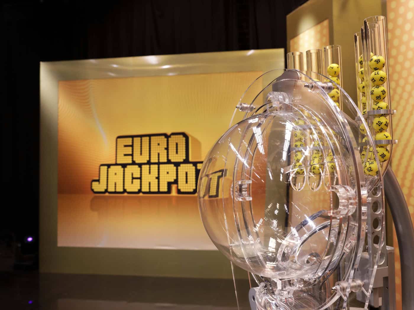 Eurojackpot-Ziehungsstudio. Vorne ist das Ziehungsgerät zu sehen, hinten ein Bildschirm mit dem Eurojackpot-Logo.