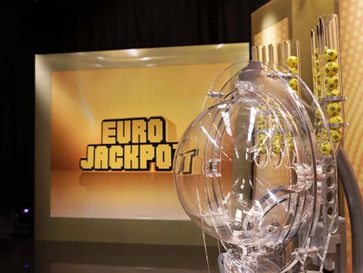 Eurojackpot-Ziehungsstudio. Vorne ist das Ziehungsgerät zu sehen, hinten ein Bildschirm mit dem Eurojackpot-Logo.