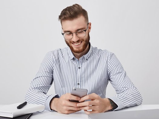 Mann mit Smartphone und Laptop am Schreibtisch