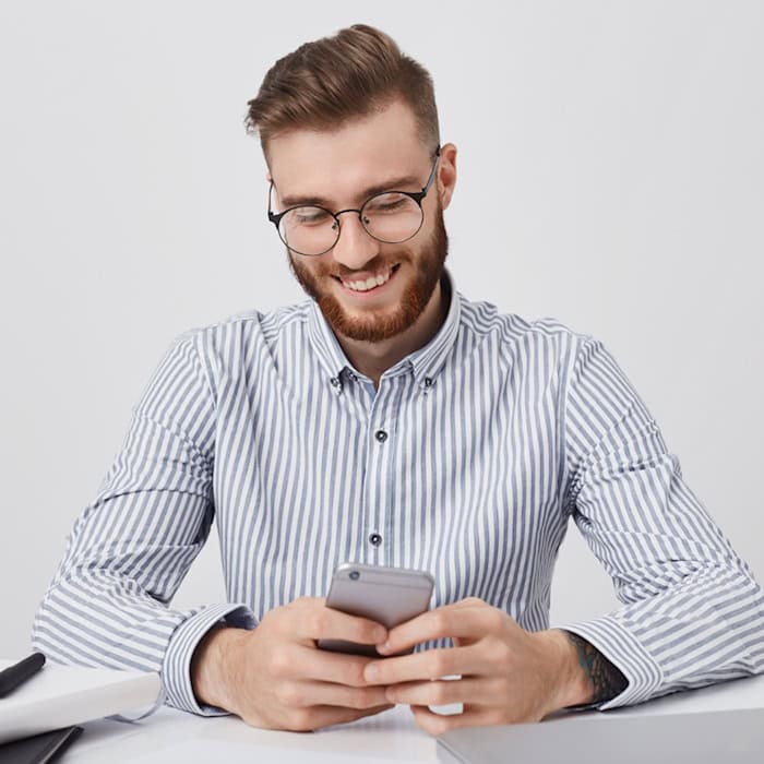 Mann mit Smartphone und Laptop am Schreibtisch