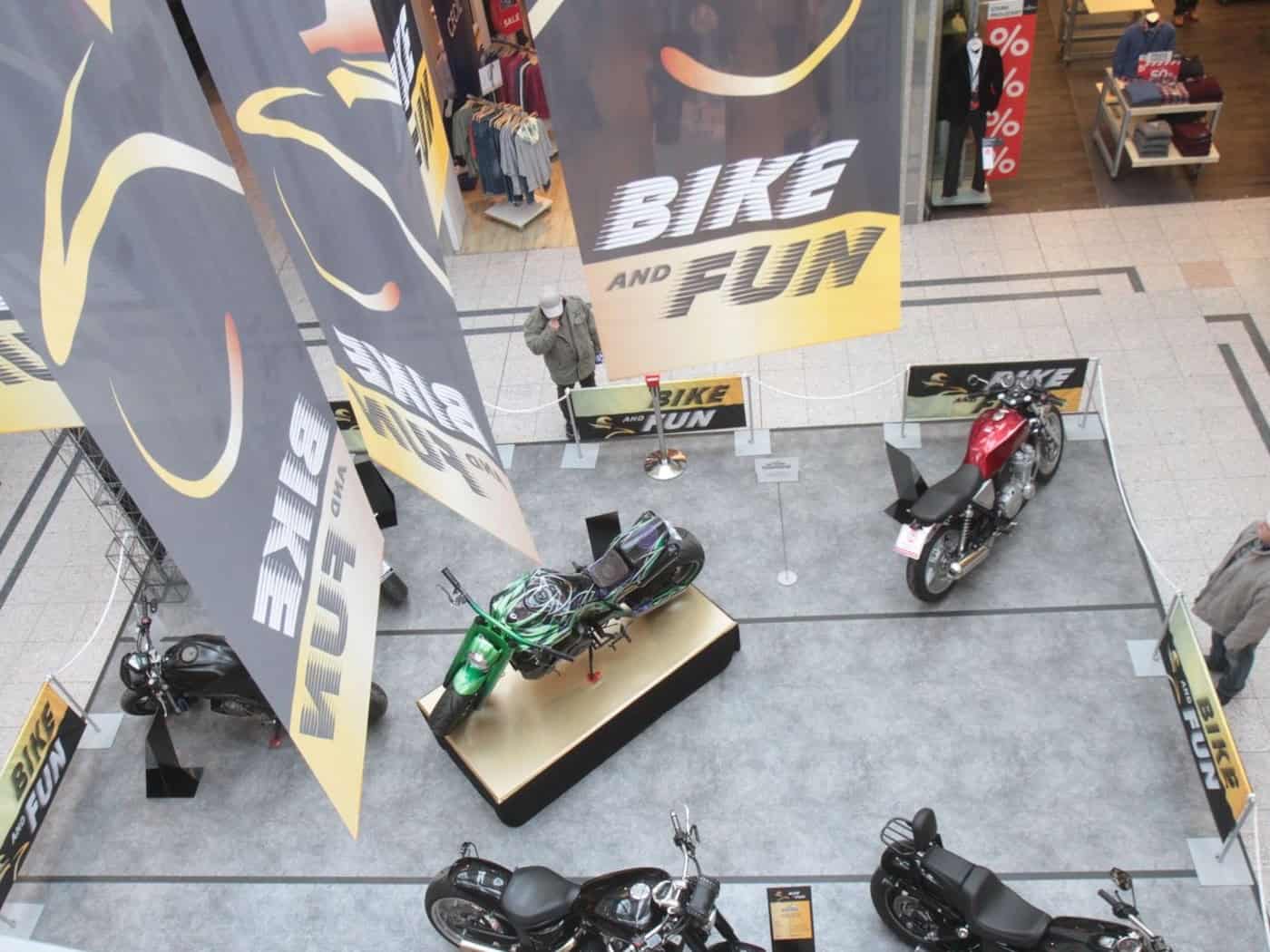 Leicht erhöhe Fläche mit mehreren ausgestellten Motorrädern, darüber hängende Banner mit der Aufschrift "Bike and Fun"
