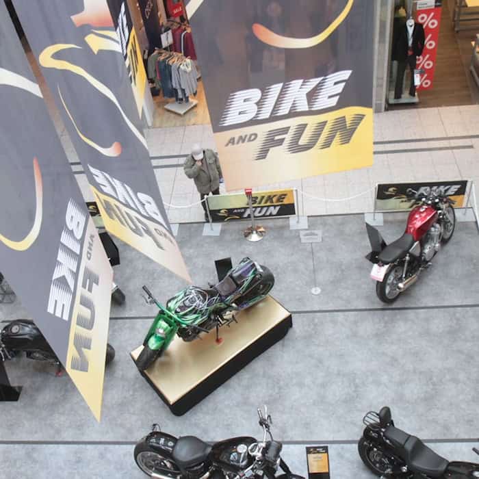 Leicht erhöhe Fläche mit mehreren ausgestellten Motorrädern, darüber hängende Banner mit der Aufschrift "Bike and Fun"