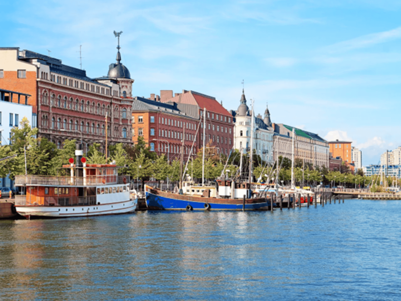 Historische bunte Häuserzeile am Wasser mit Segelschiffen und einem Dampfschiff im Hafen von Helsinki.