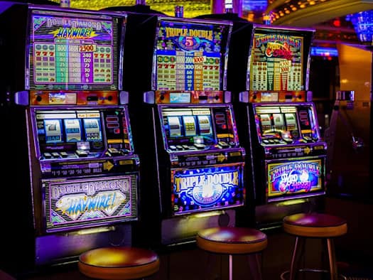 Drei leuchtende Spielautomaten mit bunten Displays und Spielnamen wie "Double Diamond" und "Triple Double" in einem Casino.