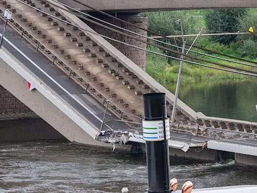 Blick auf die eingestürzte Carolabrücke in Dresden: Ein großes Brückensegment ist in die Elbe gesackt, die Gleise hängen in der Luft. Im unteren Vordergrund ist der Schornstein eines vorbeifahrenden Schiffes zu sehen.