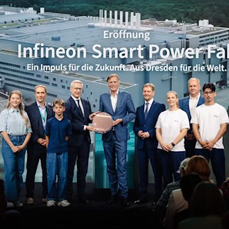 Neun Personen stehen auf einer Bühne vor einer großen Leinwand mit der Aufschrift „Eröffnung Infineon Smart Power Fab“. In der Mitte halten zwei Männer eine runde Halbleiter-Siliziumscheibe (Wafer). Im Vordergrund ist das Publikum von hinten zu sehen.