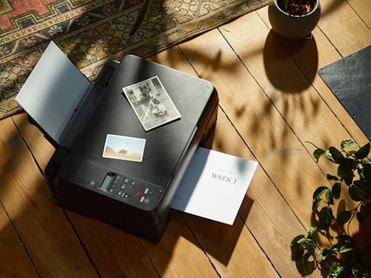 Drucker auf einem Holzboden mit ausgedruckten Fotos und Dokumenten – nachhaltiges Drucken im heimischen Umfeld.
