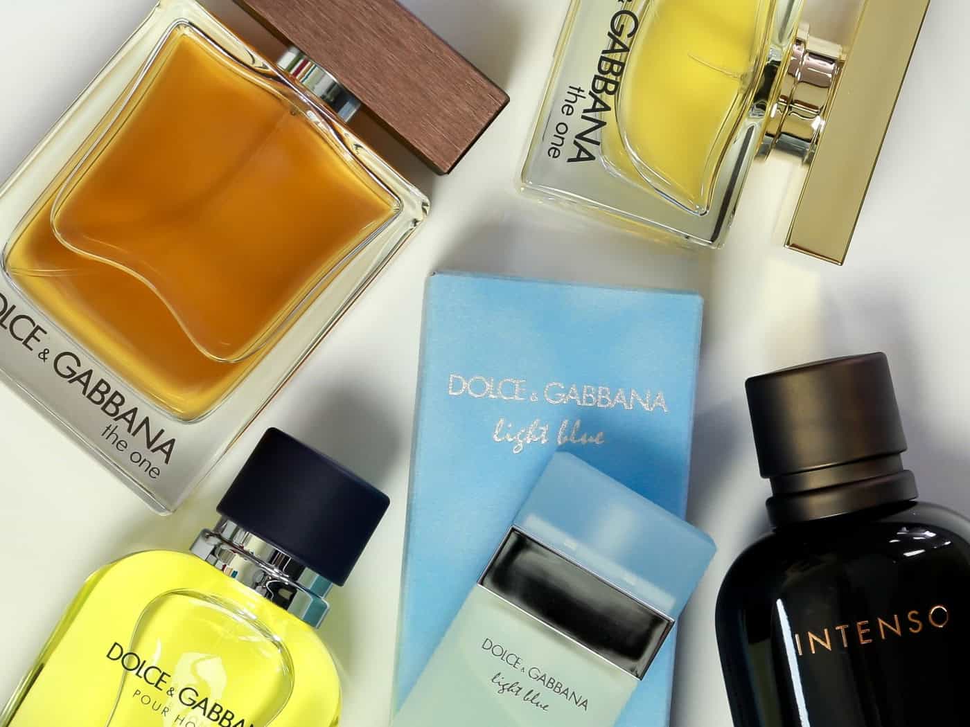 Draufsicht auf mehrere Parfümflaschen und Verpackungen der Marke Dolce & Gabbana auf weißem Grund. Zu sehen sind gelbe und bernsteinfarbene Flakons sowie eine hellblaue Schachtel und ein schwarzes Parfümfläschchen mit der Aufschrift „Intenso“.