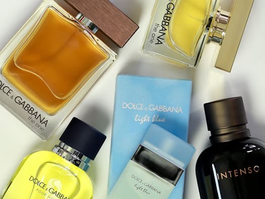 Draufsicht auf mehrere Parfümflaschen und Verpackungen der Marke Dolce & Gabbana auf weißem Grund. Zu sehen sind gelbe und bernsteinfarbene Flakons sowie eine hellblaue Schachtel und ein schwarzes Parfümfläschchen mit der Aufschrift „Intenso“.