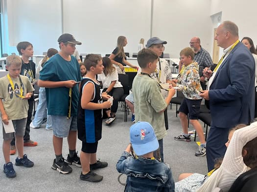 Dresdens OB Dirk Hilbert im blauen Anzug verteilt in einem hellen Saal Autogramme an eine Gruppe von Grundschulkindern, die geduldig im Kreis um ihn anstehen und gespannt warten.