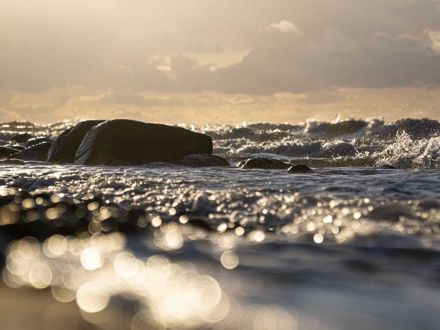 Goldener Sonnenuntergang über den Wellen – Felsen und glitzerndes Wasser als Symbol für Erholung und Weite.