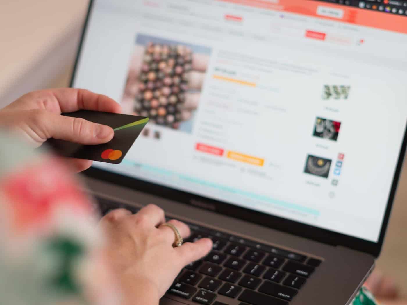 Hand hält Kreditkarte über Laptop mit E-Commerce-Website