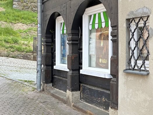 Detailaufnahme der Ecke eines Umgebindehauses in eher schlechtem baulichen Zustand, in den Fenstern Plakate mit Werbung