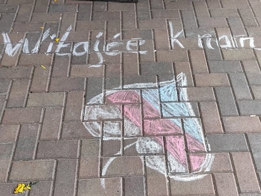 Auf einem Fußweg stehen mit Kreide die Worte „Witajće k nam“, darunter ein gezeichnetes Lindenblatt