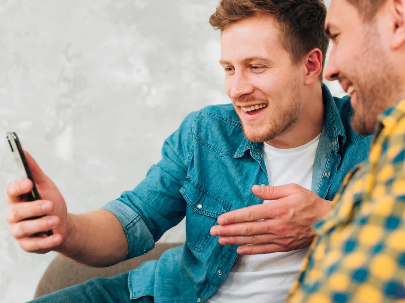 Zwei Männer sitzen zusammen, einer hält ein Smartphone