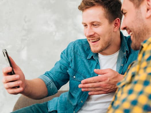 Zwei Männer sitzen zusammen, einer hält ein Smartphone