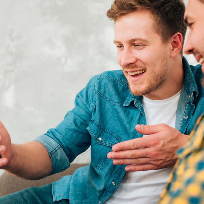 Zwei Männer sitzen zusammen, einer hält ein Smartphone