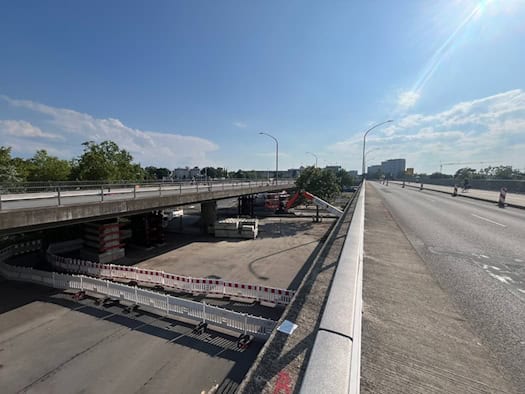 Blick über die Brücke Budapester Straße in Dresden bei Sonnenschein. Auf der linken Seite ist der Unterbau mit rot-weißen Zäunen abgesperrt und durch Notstützen gesichert, wo Messungen und Arbeiten an der maroden Betonkonstruktion stattfinden.