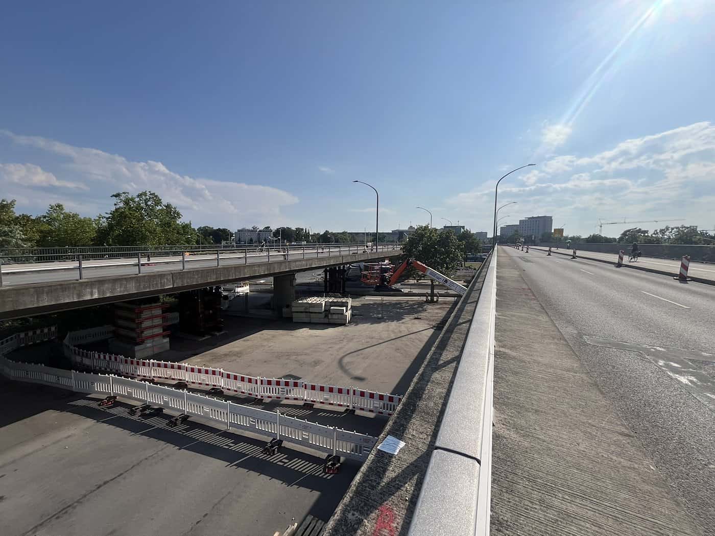 Blick über die Brücke Budapester Straße in Dresden bei Sonnenschein. Auf der linken Seite ist der Unterbau mit rot-weißen Zäunen abgesperrt und durch Notstützen gesichert, wo Messungen und Arbeiten an der maroden Betonkonstruktion stattfinden.
