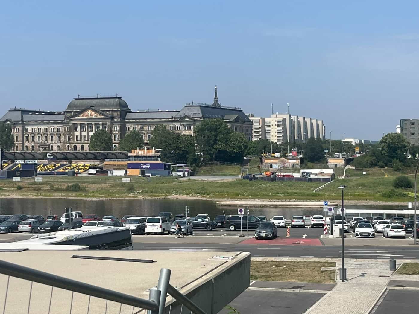 Blick über einen Parkplatz am Elbufer auf die Elbe in Dresden. Am gegenüberliegenden Ufer steht das historische Finanzministerium. Rechts sind die freien Anschlüsse der abgetragenen Carolabrücke im Elbtal zu sehen.