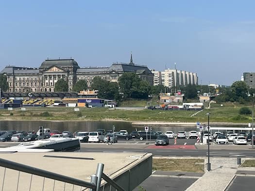 Blick über einen Parkplatz am Elbufer auf die Elbe in Dresden. Am gegenüberliegenden Ufer steht das historische Finanzministerium. Rechts sind die freien Anschlüsse der abgetragenen Carolabrücke im Elbtal zu sehen.