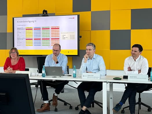 Pressekonferenz zum Carolabrücke-Neubau vor gelb-grauer Wand: Anke Lietzmann, Steven Eichler, Baubürgermeister Stephan Kühn und Stadtsprecher Daniel Heine am Tisch (v.l.). Ein Monitor im Hintergrund zeigt die Ergebnisse der Kinderbeteiligung.
