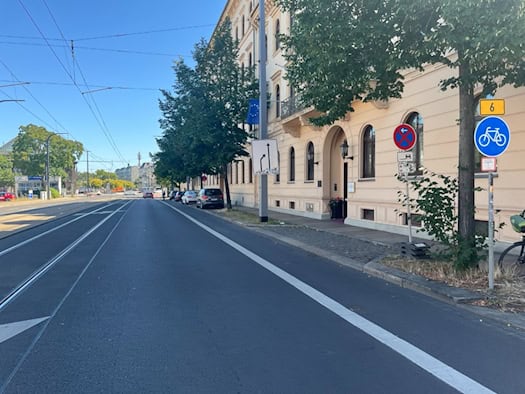 Blick auf die Antonstraße in Dresden mit Fahrbahn, Straßenbahnschienen und Fahrradweg. Auf der rechten Seite stehen historische Gebäude, Straßenbäume sowie Verkehrsschilder, darunter ein blaues Radweg-Schild.