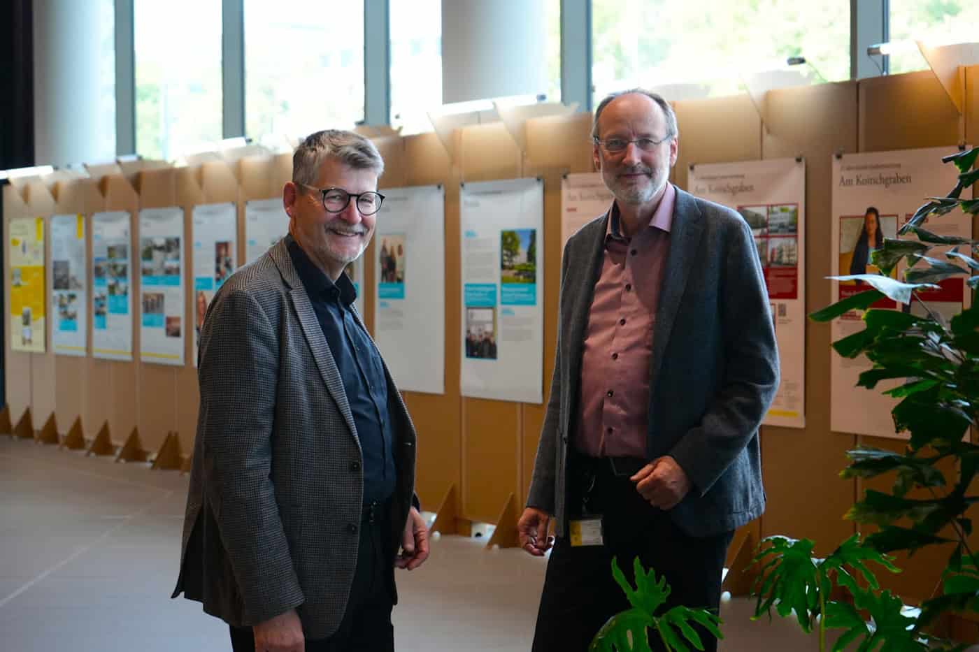 Dr. Matthias Lerm und Thomas Pieper stehen lächelnd im Stadtforum Dresden vor Plakaten der Begleitausstellung „25 Jahre Soziale Stadt“. Sie repräsentieren das Amt für Stadtplanung und Mobilität.