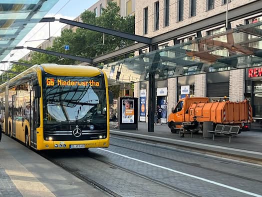 Ein gelber Linienbus der DVB mit der Anzeige „68 Niederwartha“ steht an einer überdachten Haltestelle in Dresden. Fahrgäste warten auf dem Bahnsteig, im Hintergrund ist ein Gebäude mit REWE-Filiale zu sehen.