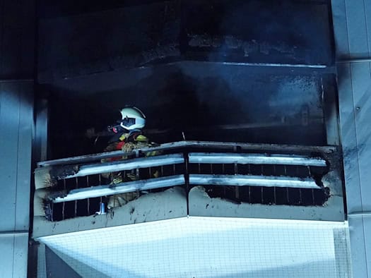 Ein Atemschutzgeräteträger der Feuerwehr steht bei Nacht auf dem stark verrußten und beschädigten Balkon eines Hochhauses in Dresden-Gruna, um den Brandort nach dem Feuer zu kontrollieren.