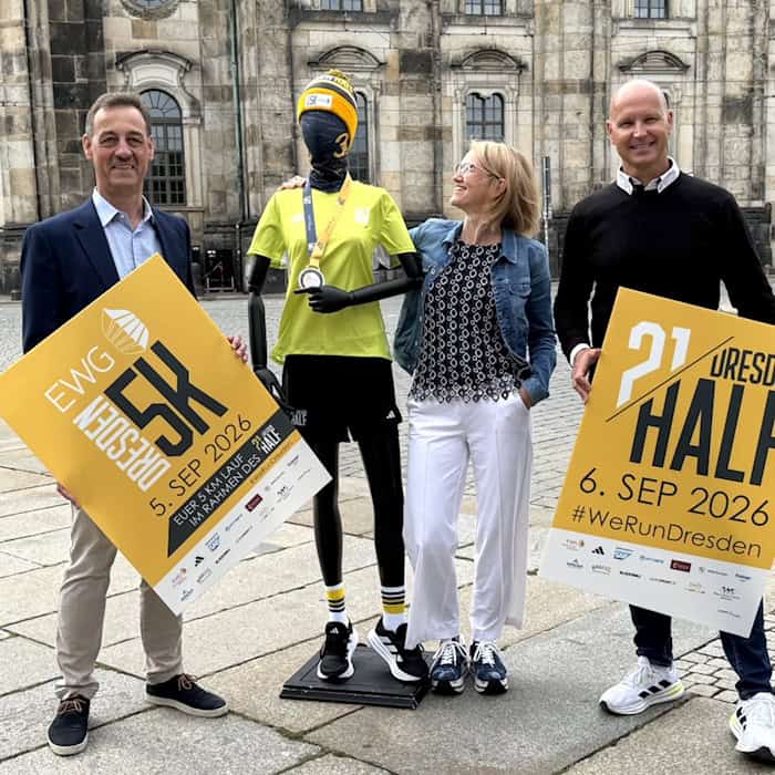 Michael Reichel, Antje Neelmeijer und André Egger halten Plakate für den DresdenHALF und EWG Dresden5K. Zwischen ihnen steht eine Schaufensterpuppe in Laufbekleidung vor Altstadtkulisse.