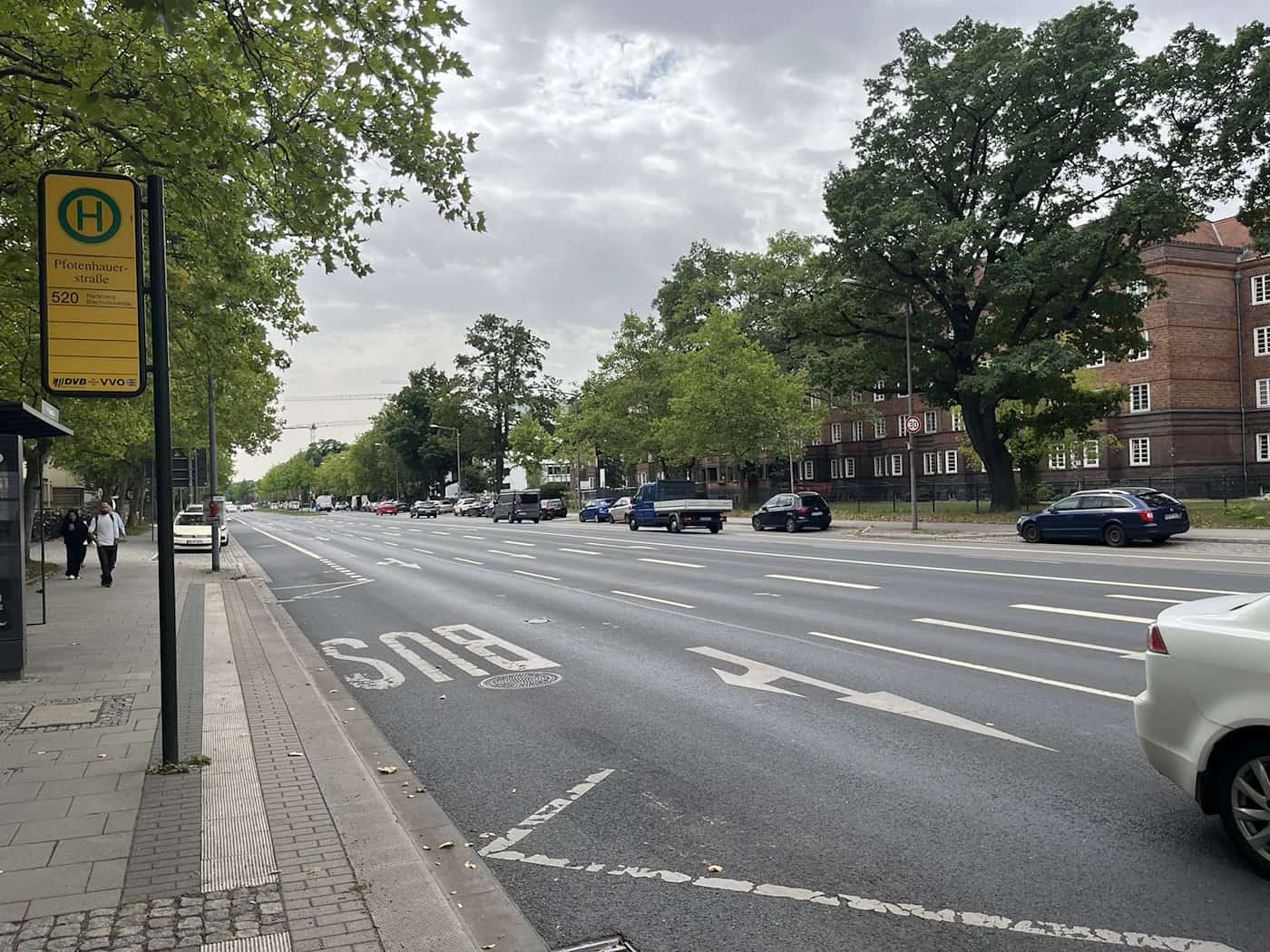 Straßenszene an der Fetscherstraße in Dresden auf Höhe der Bushaltestelle Pfotenhauerstraße. Im Vordergrund steht ein gelbes DVB-Haltestellenschild, dahinter erstreckt sich die mehrspurige Asphaltstraße.