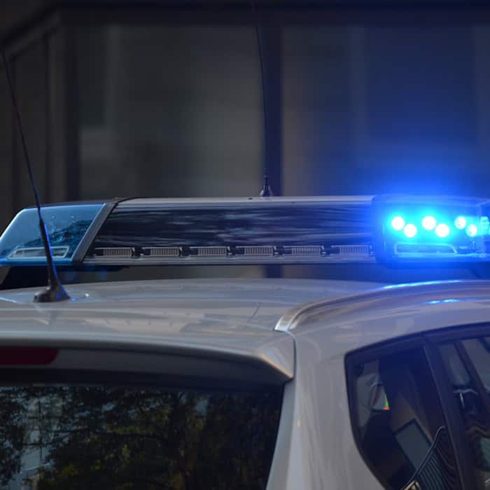 Nahaufnahme eines Polizeifahrzeugs bei Nacht. Die blaue Signalleuchte auf dem Dach des Streifenwagens leuchtet hell im Dunkeln.