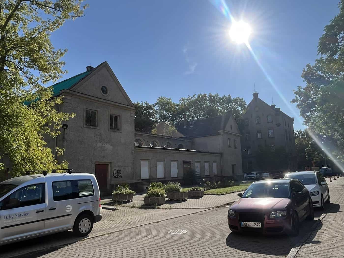 Sonniger Hofbereich mit geparkten Autos vor alten, teilweise verriegelten Nebengebäuden und dem denkmalgeschützten Hauptgebäude an der Löbtauer Straße in Dresden-Friedrichstadt.