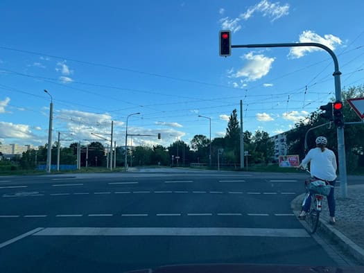 Blick vom Seidnitzer Weg über die mehrspurige Kreuzung der Mügelner Straße zur Gamigstraße. Rechts wartet eine Radfahrerin bei Rot an der Ampel.