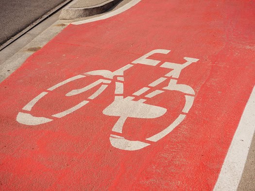 Ein weiß aufgemaltes Fahrradsymbol auf einem leuchtend rot markierten Radfahrstreifen auf dem Asphalt neben einer Bordsteinkante.