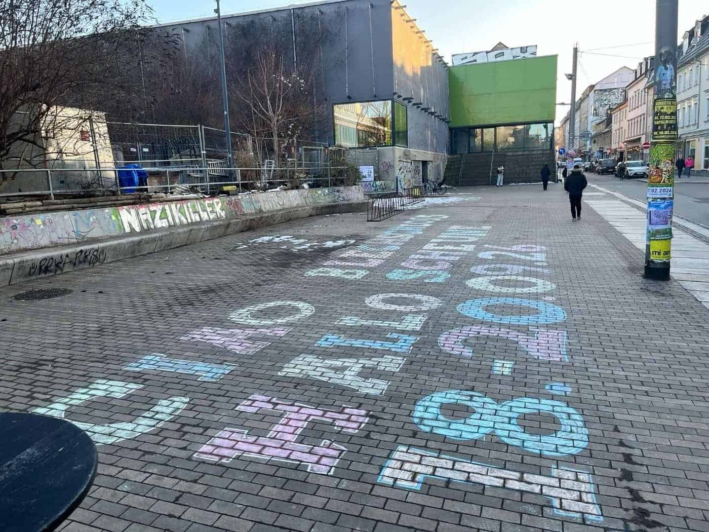 Bunte Kreideschrift auf dem Pflaster vor dem Scheune-Gebäude in der Dresdner Neustadt: „CIAO BLECHSCHLOSS HALLO SCHEUNE 18.-20.09.26“. Im Hintergrund ist das sanierten Gebäude mit der auffälligen grünen Eingangsnische zu sehen.