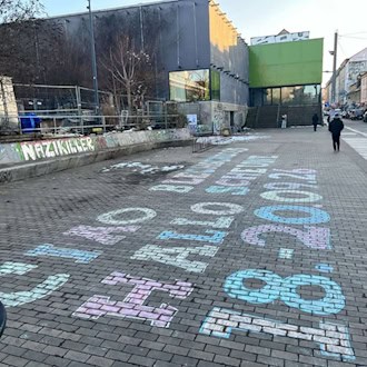 Bunte Kreideschrift auf dem Pflaster vor dem Scheune-Gebäude in der Dresdner Neustadt: „CIAO BLECHSCHLOSS HALLO SCHEUNE 18.-20.09.26“. Im Hintergrund ist das sanierten Gebäude mit der auffälligen grünen Eingangsnische zu sehen.