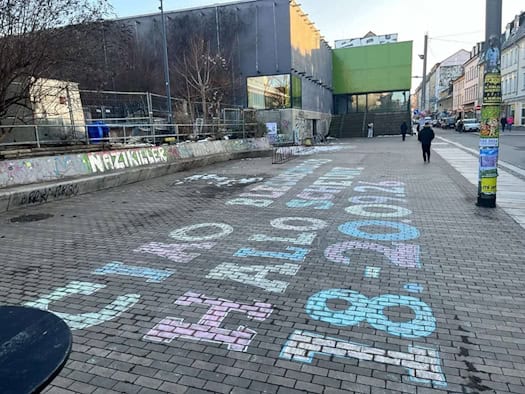 Bunte Kreideschrift auf dem Pflaster vor dem Scheune-Gebäude in der Dresdner Neustadt: „CIAO BLECHSCHLOSS HALLO SCHEUNE 18.-20.09.26“. Im Hintergrund ist das sanierten Gebäude mit der auffälligen grünen Eingangsnische zu sehen.