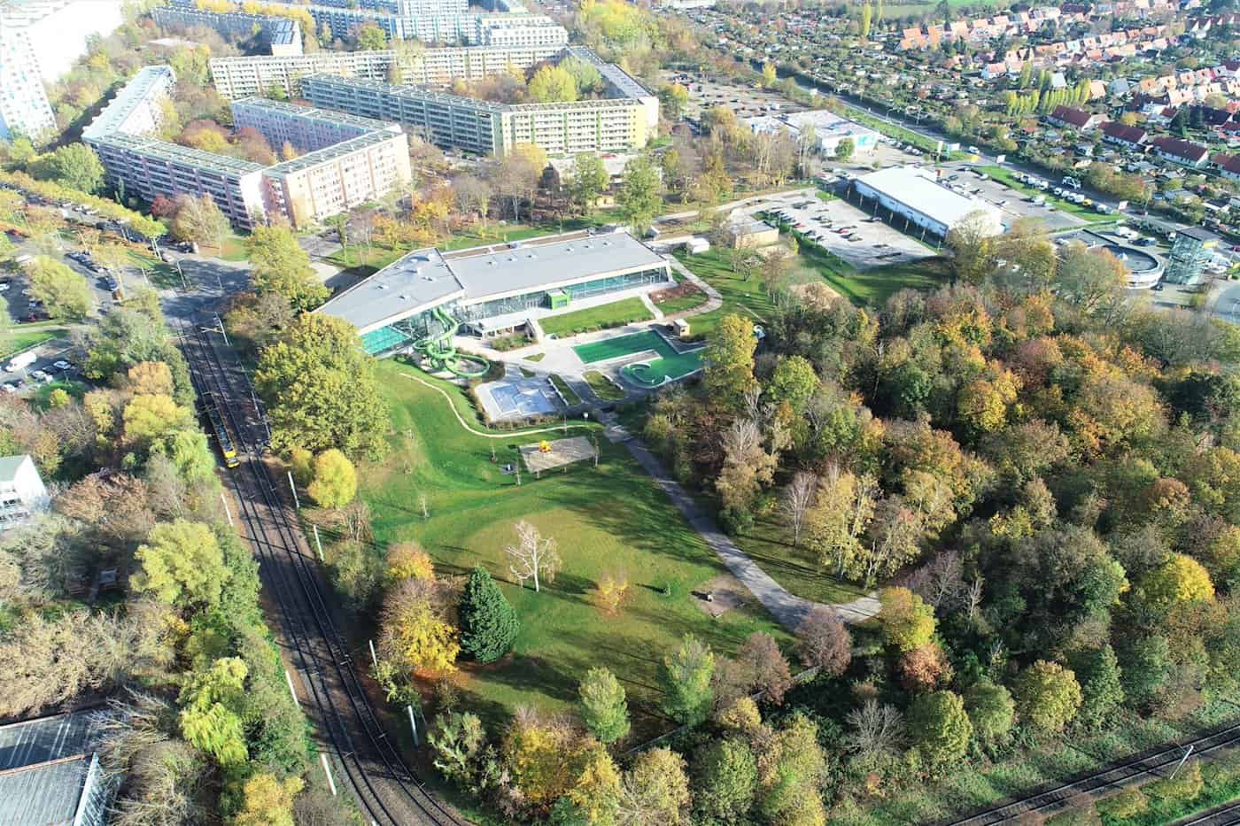 Luftbild des modernisierten Kombibads Prohlis in Dresden mit Außenbecken, Wasserrutsche, Liegewiesen und angrenzenden Straßenbahnschienen sowie Plattenbauten im Hintergrund.