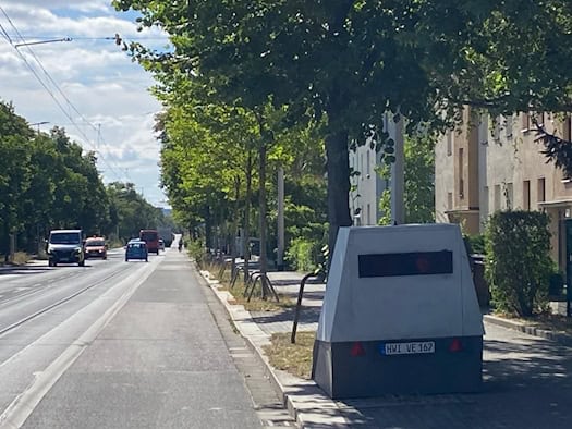 Grauer mobiler Messanhänger mit Kennzeichen HWI VE 167 steht auf dem Gehweg unter Bäumen an einer Straße in Dresden. Auf der mehrspurigen Fahrbahn daneben rollt der Verkehr.