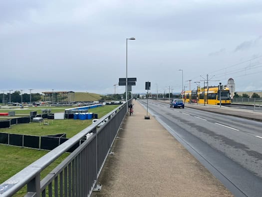 Blick von einer Brücke auf das Veranstaltungsgelände der RINNE Dresden im Ostragehege mit Absperrungen und Mobiltoiletten für das Konzert der Toten Hosen. Rechts fährt eine gelbe Straßenbahn der DVB.