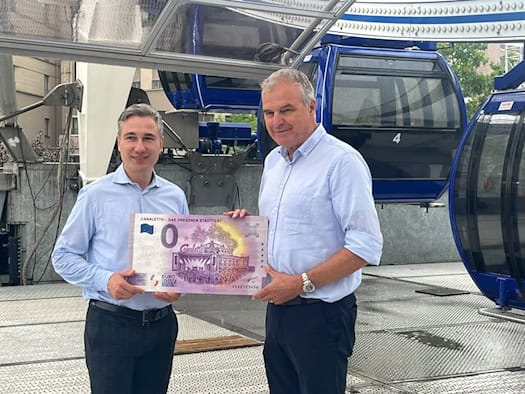 Baubürgermeister Stephan Kühn und Riesenrad-Betreiber Oscar Bruch halten gemeinsam einen übergroßen Null-Euro-Souvenirschein des Canaletto-Stadtfests vor blauen Riesenrad-Gondeln.