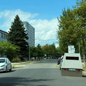 Ein grauer Blitzeranhänger mit dem Kennzeichen HWI VE 167 steht am rechten Straßenrand der Josephinenstraße in Dresden. Rechts daneben steht ein gelbes Umleitungsschild, links ist ein Schulgebäude und ein weißes Auto zu sehen.