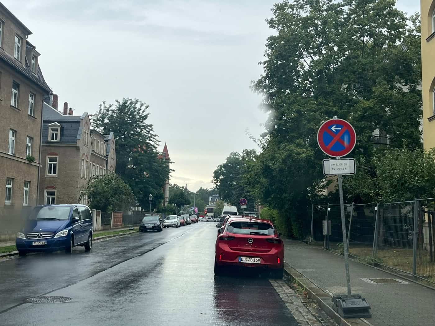 Ein temporäres absolutes Halteverbotsschild am Straßenrand der nassen Bellingrathstraße in Dresden. Das Zusatzschild weist auf ein Halteverbot am 21.08.26 hin. Im Hintergrund stehen geparkte Autos vor Wohnhäusern.
