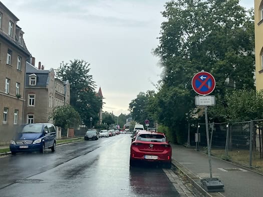 Ein temporäres absolutes Halteverbotsschild am Straßenrand der nassen Bellingrathstraße in Dresden. Das Zusatzschild weist auf ein Halteverbot am 21.08.26 hin. Im Hintergrund stehen geparkte Autos vor Wohnhäusern.