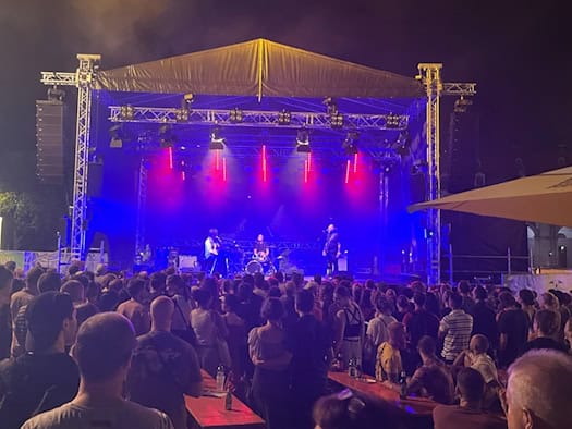 Menschenmenge vor einer beleuchteten Open-Air-Bühne bei Nacht auf dem Dresdner Stadtfest. Die Band spielt unter blauem und rotem Licht, während die Zuschauer dicht gedrängt vor der Bühne stehen und an Tischen sitzen. 